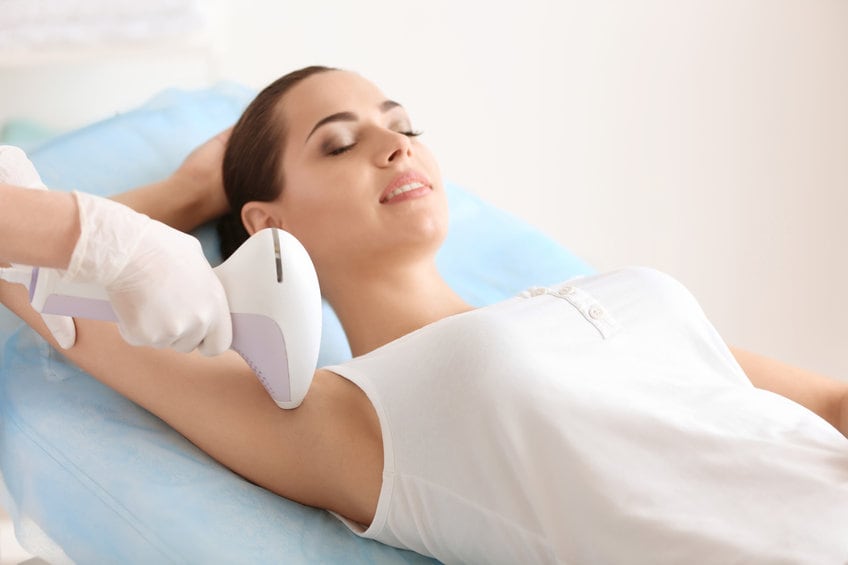 Femme utilisant un épilateur à lumière pulsée sur sa jambe dans une salle de bain lumineuse