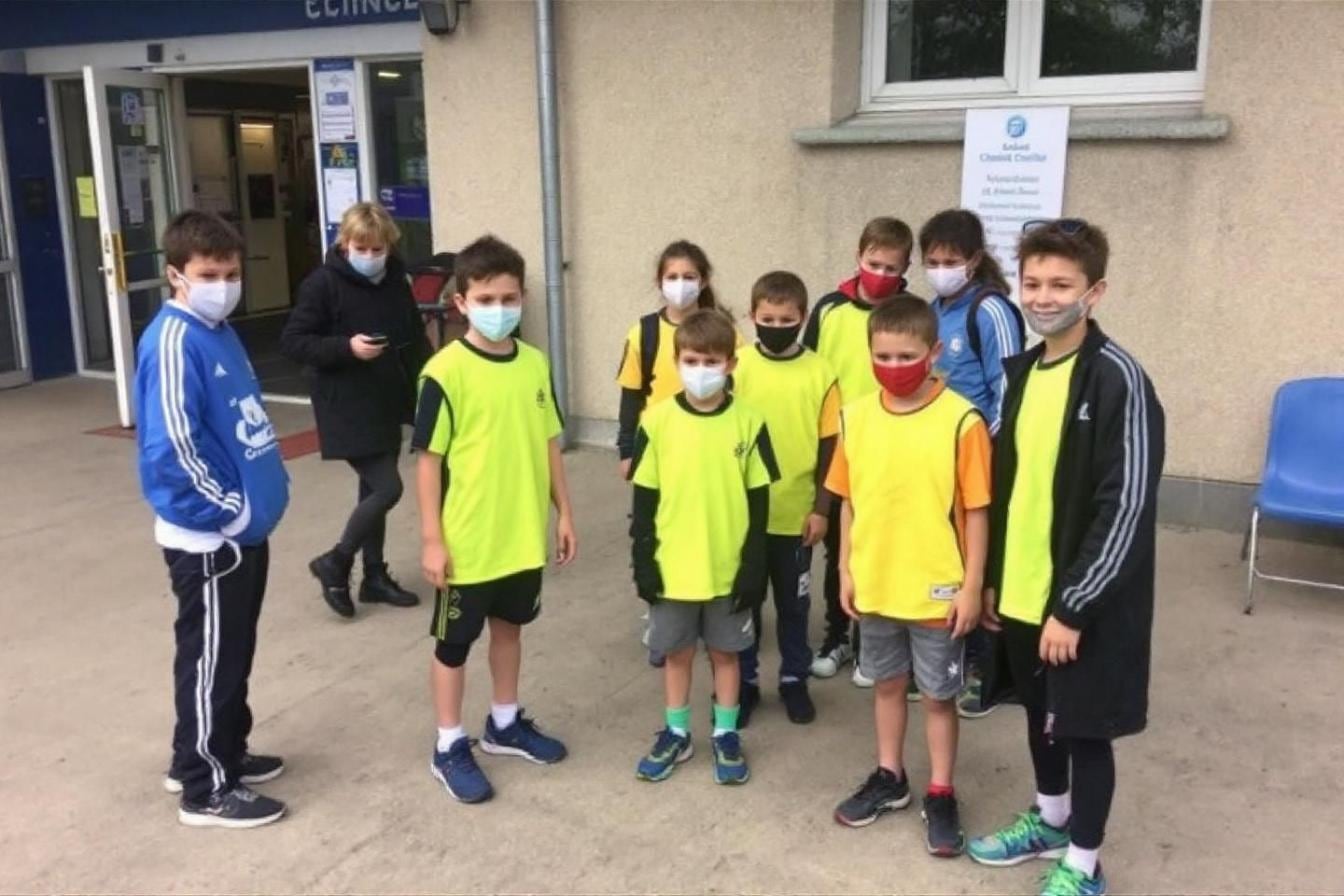 Jeune enfant en tenue de sport tenant son sac près d’un terrain, accompagné d’un parent avant une compétition de club