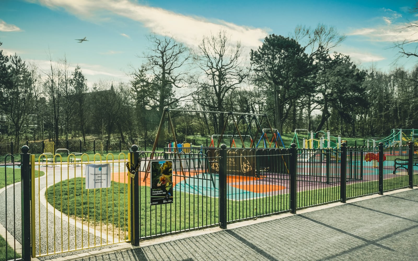 Place publique arborée avec bancs colorés, tables de jeu et modules ludiques fréquentés par des familles et des habitants