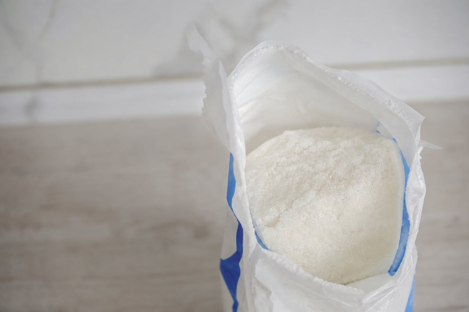 Paquet de sucre en poudre ouvert sur un plan de travail de cuisine, grains de sucre renversés, lumière naturelle
