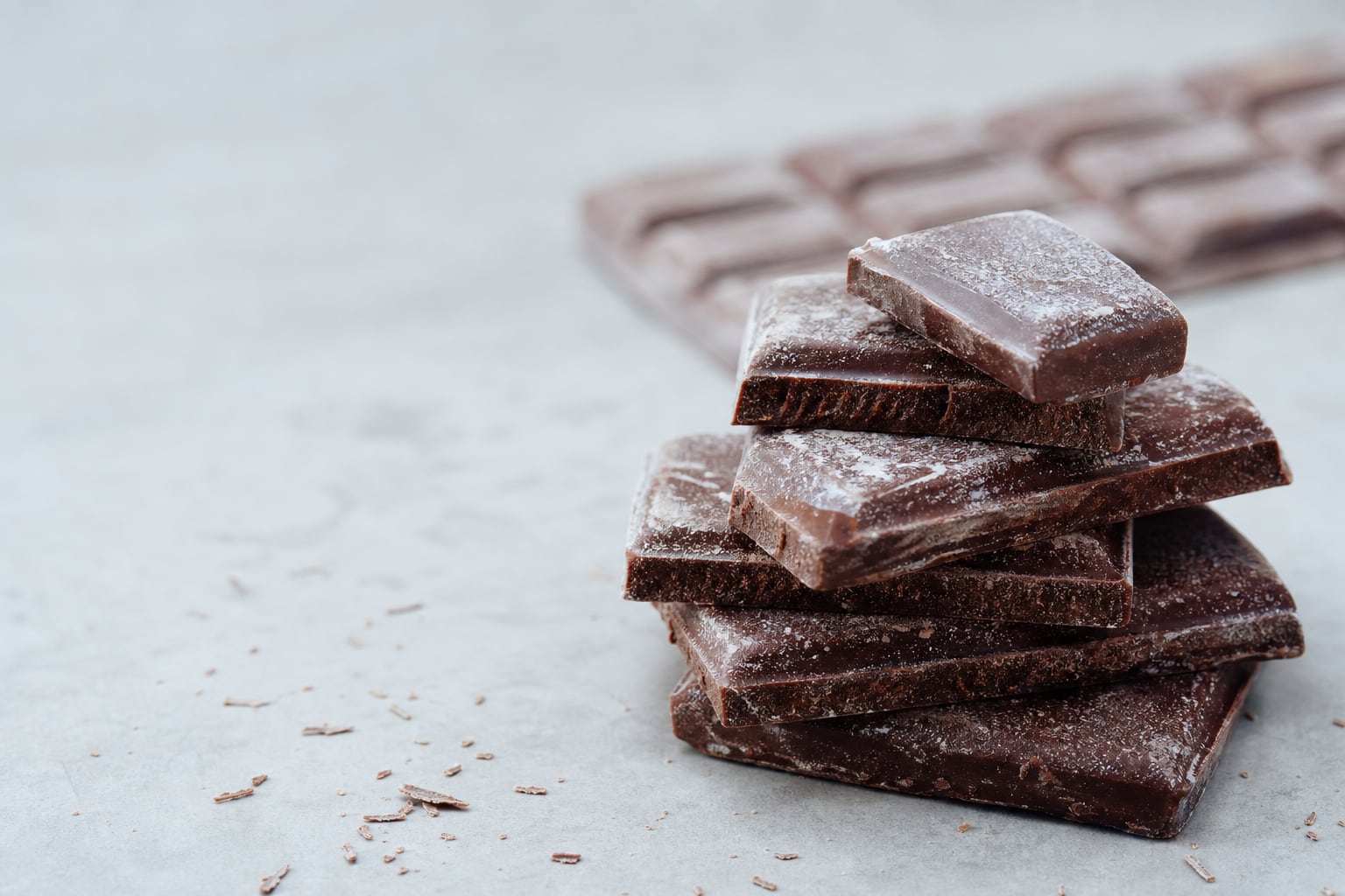 Carrés de chocolat noir cassés avec un léger voile blanchâtre en surface, éclairage naturel de cuisine