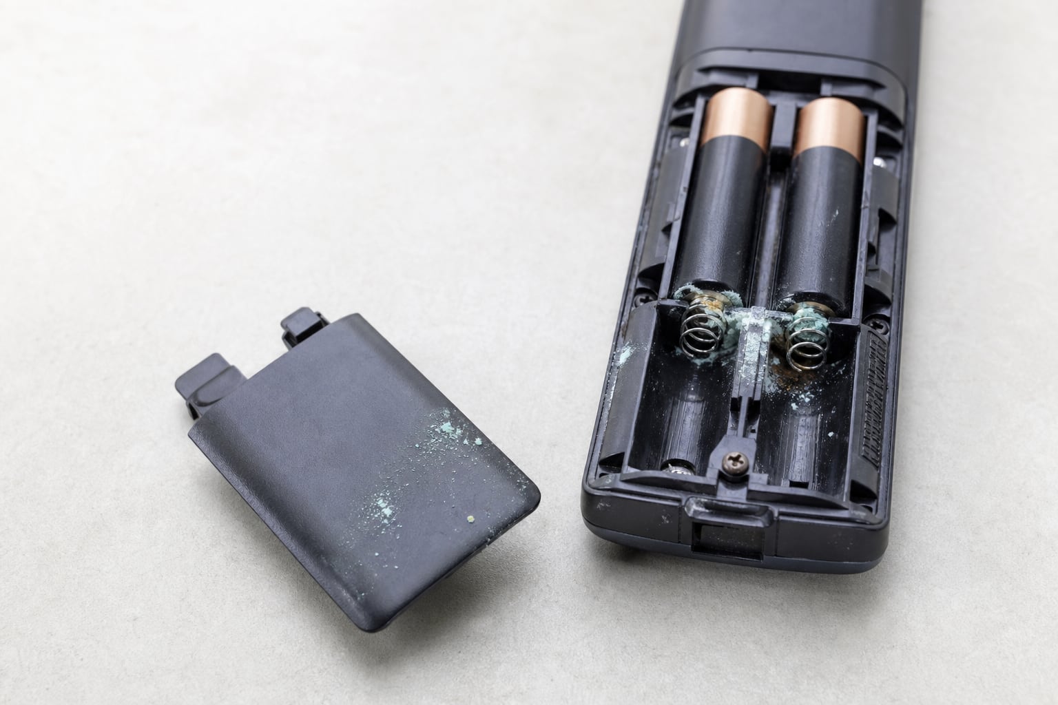 Compartiment à piles d'une télécommande ouvert, avec des dépôts blancs et verdâtres de corrosion sur les ressorts
