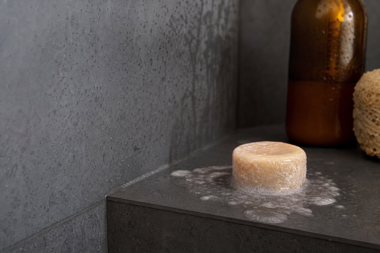 Pain de shampoing solide ramolli posé sur un porte-savon détrempé dans une douche